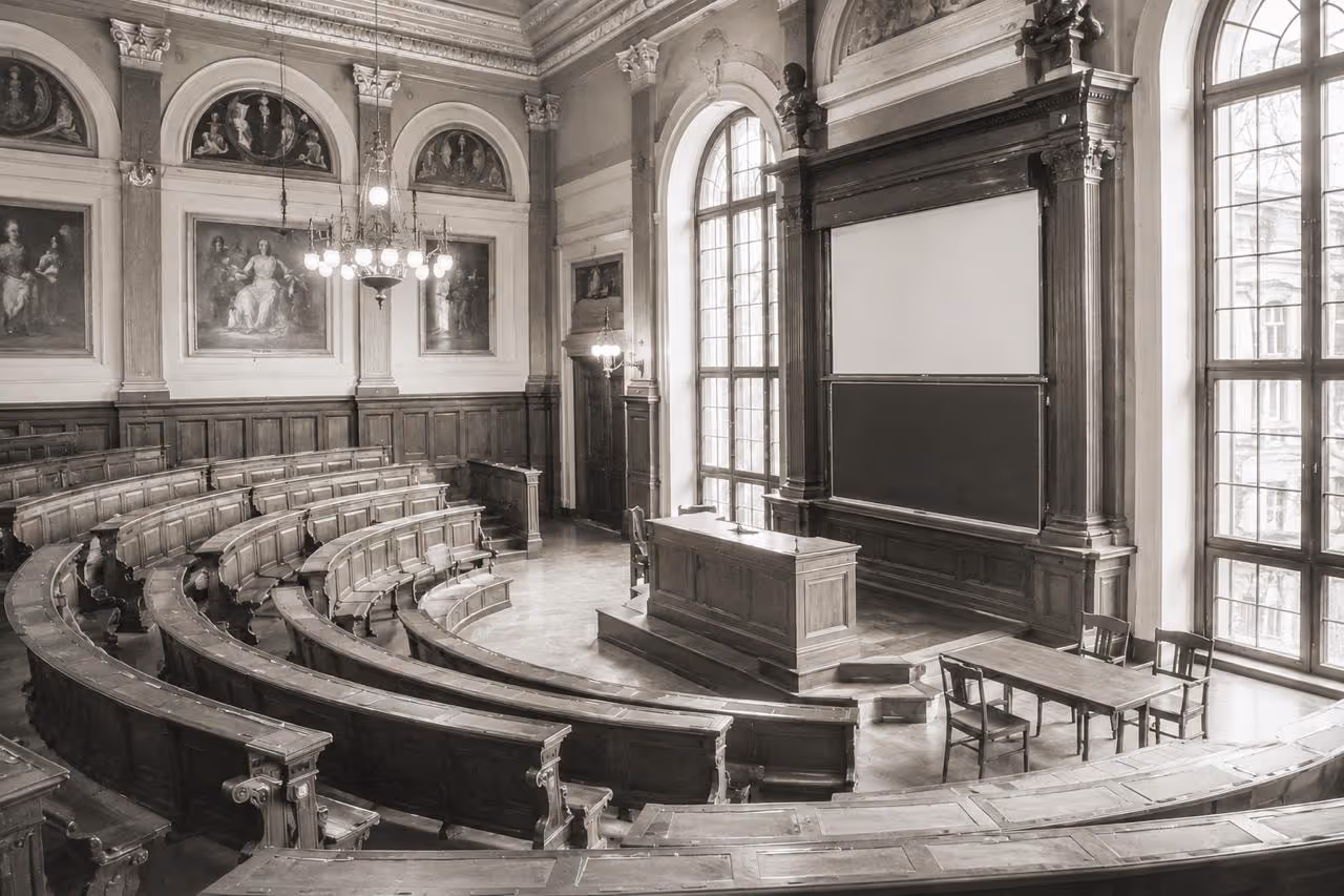 Historischer Hörsaal mit halbrund ansteigenden Sitzreihen, Rednerpult und hohen Fenstern.