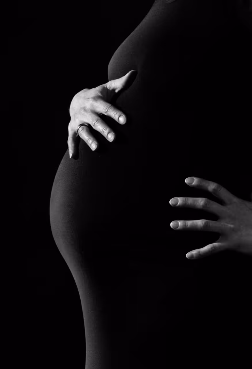 A black-and-white photograph of a pregnant belly, held gently by two hands.